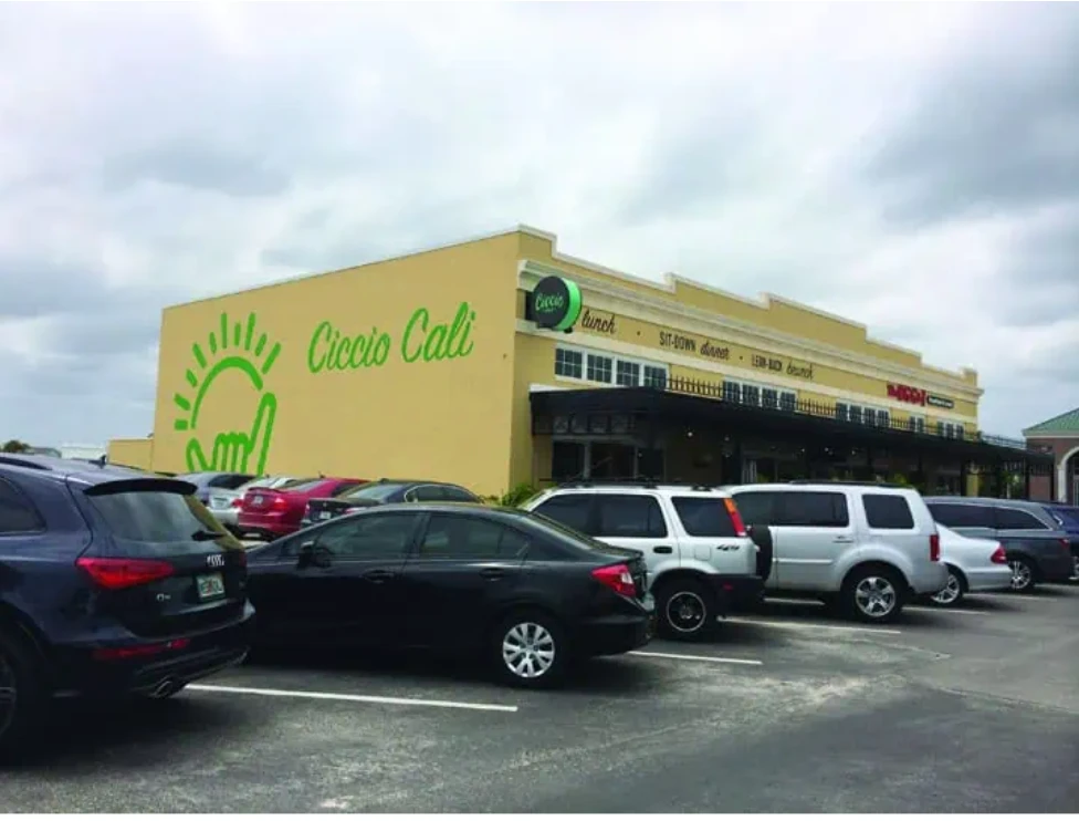 The original bright green 'Ciccio Cali' mural with the hang-ten sun logo on the side of the Winthrop restaurant, visible from the parking lot