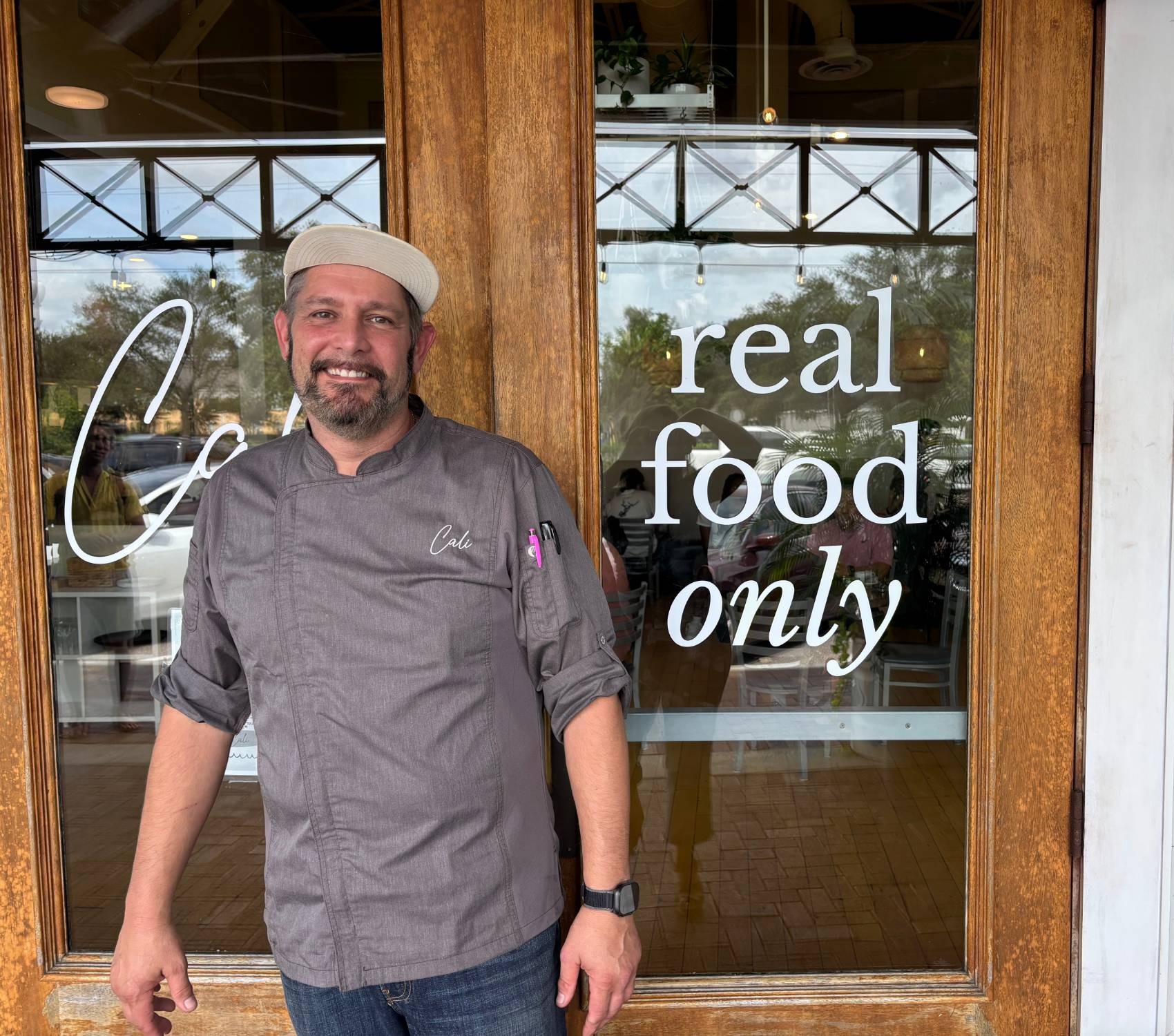 A Cali chef standing at the entrance to the Winthrop restaurant, with the restaurant's "real food only" window etching behind him