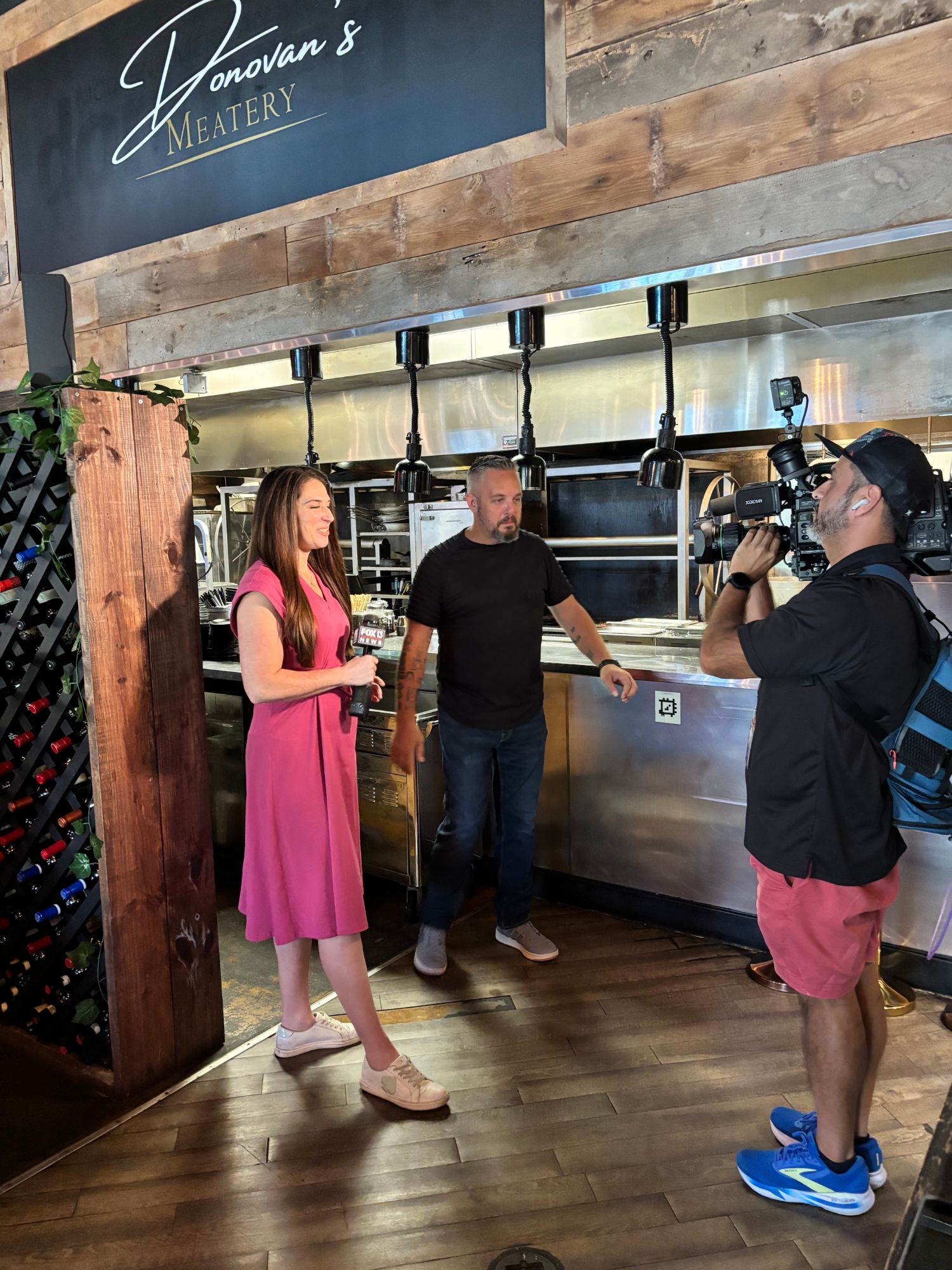 Fox 13 reporter Kellie Cowan interviewing John Camisa, owner of Donovan's Meatery, with the Donovan's sign and camera crew visible, during the live Good Morning Tampa Bay broadcast